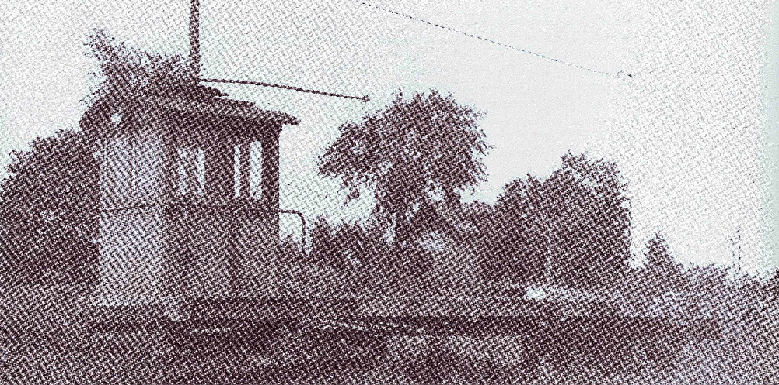 An old black and white photograph showing a trolley car on a rail line. There is a field in the background.