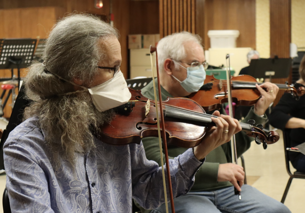 Two men in health masks play the violin. 