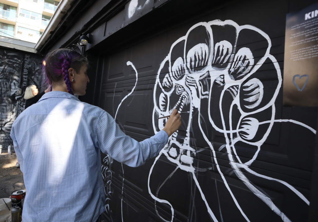 A woman paints a mural on a garage door. 