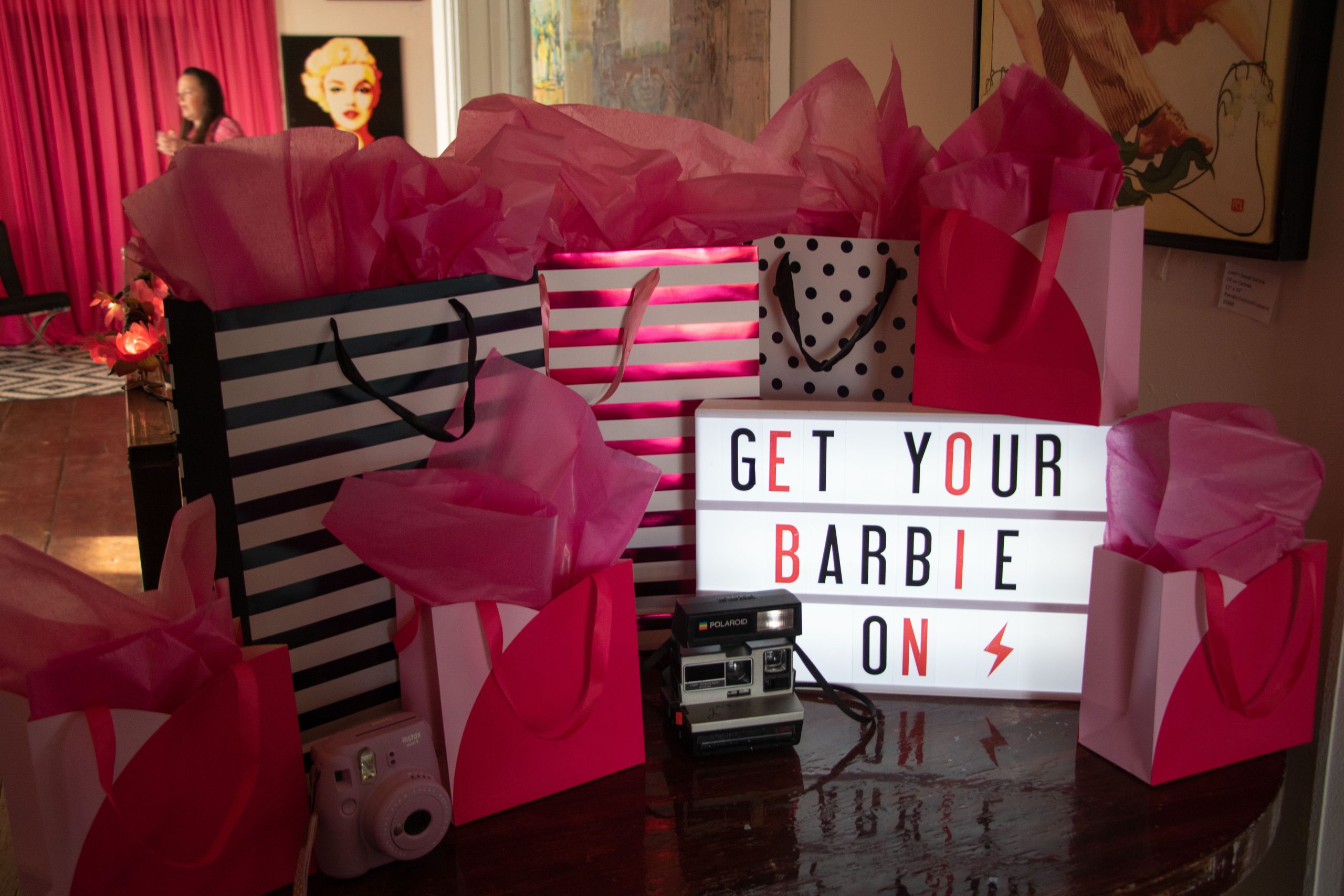 A sign reading “get your Barbie on” is surrounded by pink gift bags.