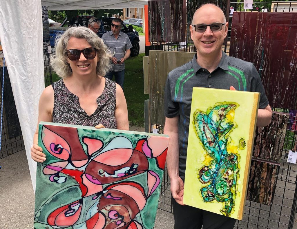 A man and a woman hood up paintings and pose for a photograph. 