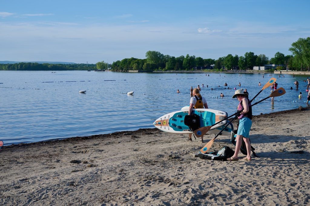 Two people carry a paddle board to the water. 