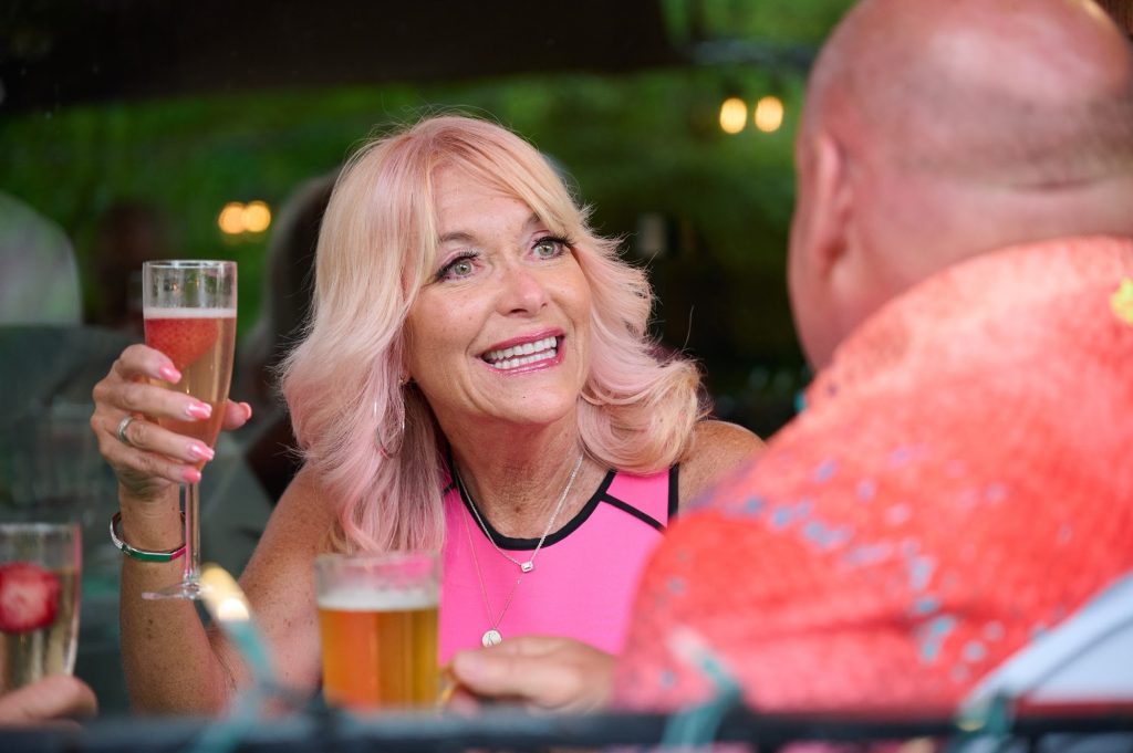 Keri whom is wearing a pink dress holds up a drink. 