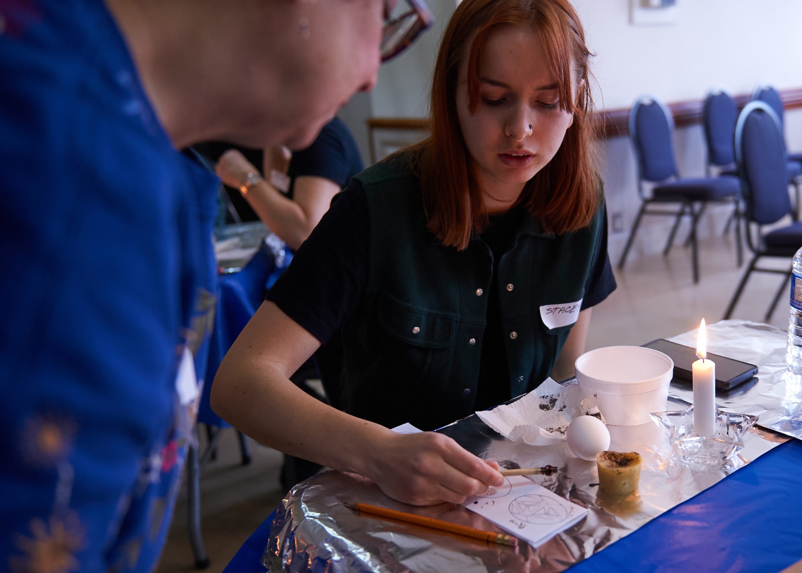 Two women look at drawings on a piece of paper. They are about to start painting the eggs.