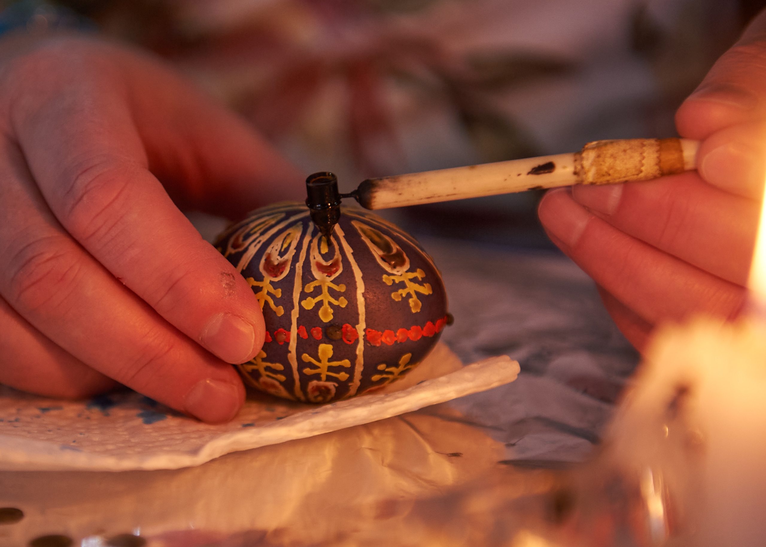 An up close photo of a dark coloured egg as a person draws designs on it.