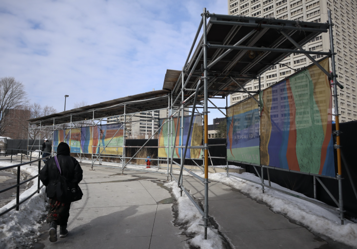 Construction scaffolding with a colourful decorative design on the right side lines the pathway at Tunney’s Pasture station.