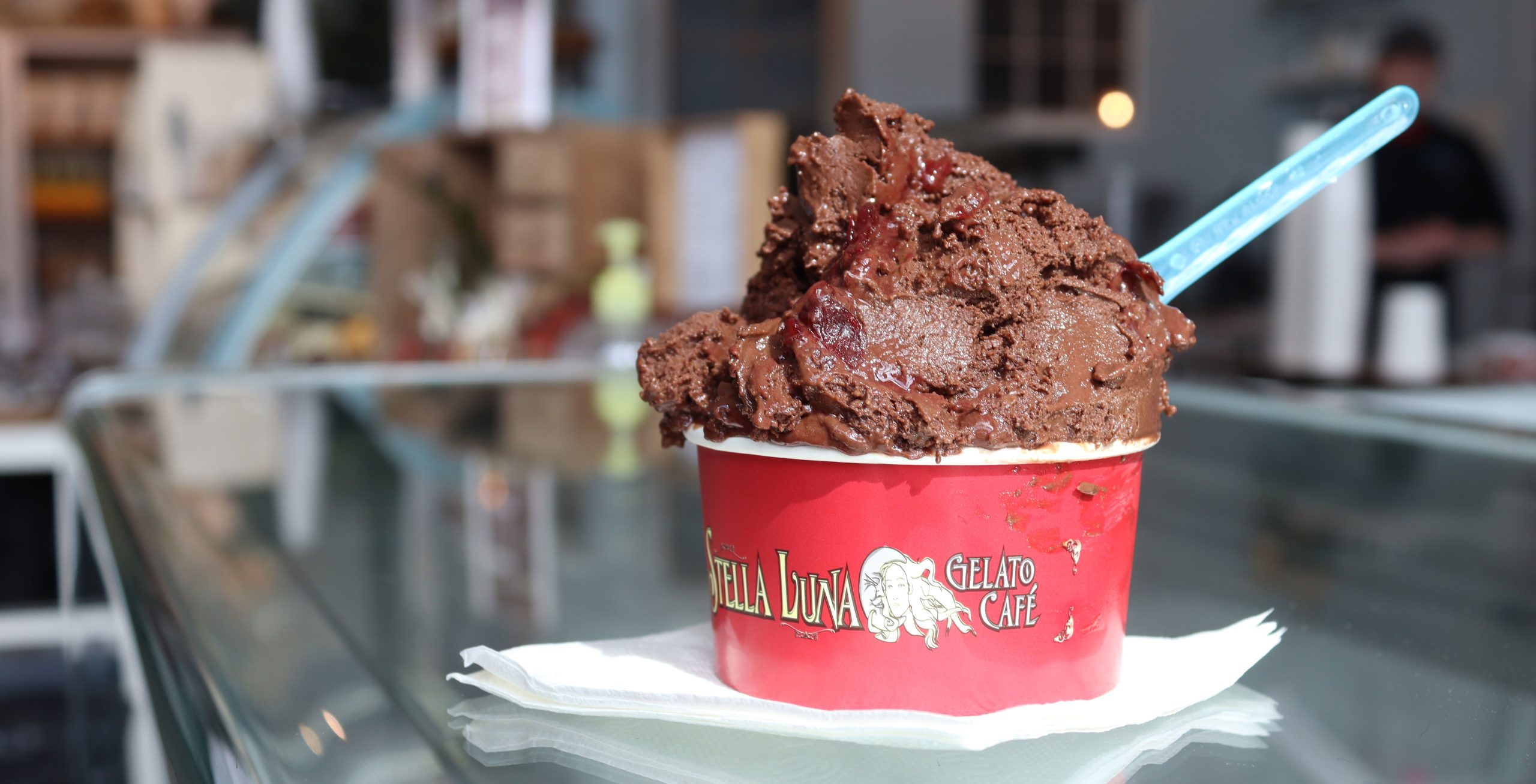 Chocolate gelato sits in a red bowl atop of a counter. 