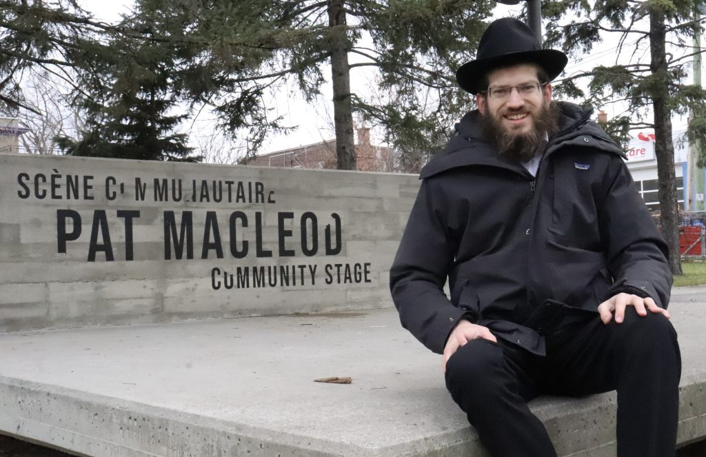 A man wearing a hat posted for a photo sitting down on a stage