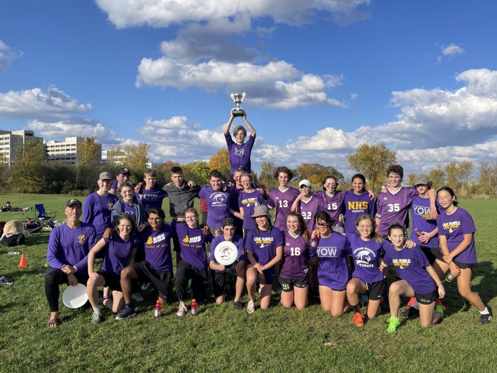 A group of students wearing purple shorts pose for on a field during a fall day.