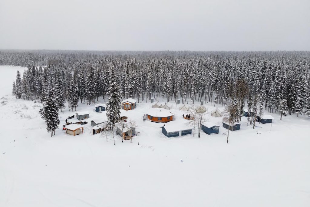 Dene Healing Camp in Fort Providence, as seen from the top of a hill. Many pine trees are in the distance with a few small buildings in the front.