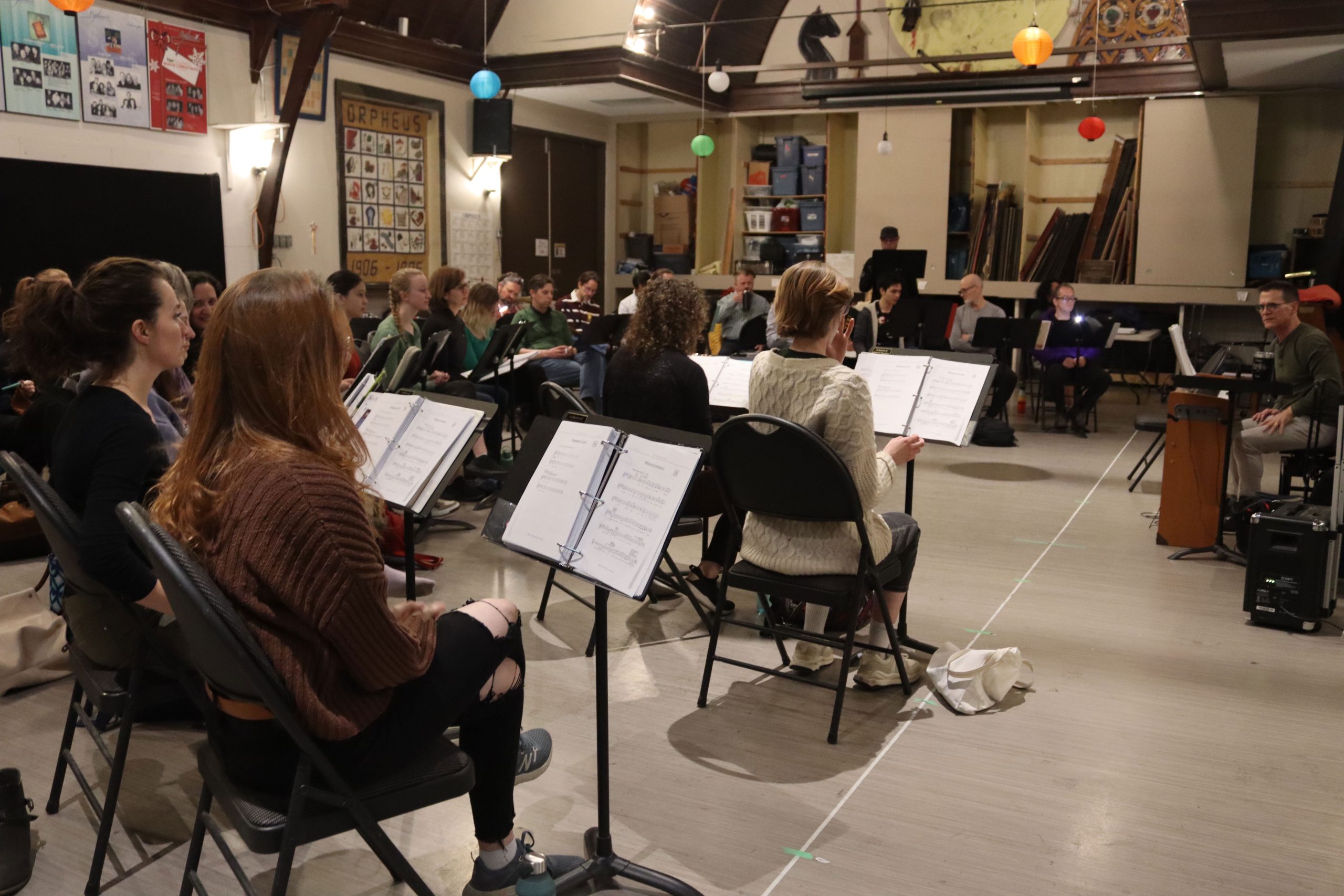 Members of Orpheus’ Something Rotten sit in front of music sheets.