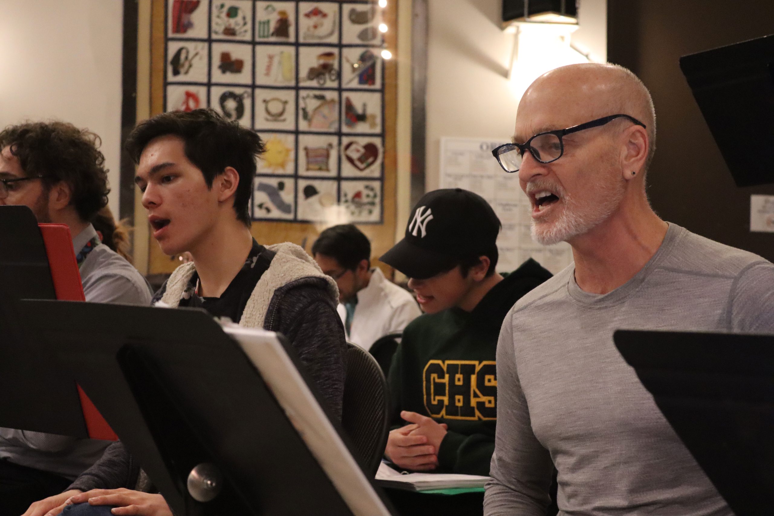 Two men sitting in the front sing while sitting in front of music sheets.