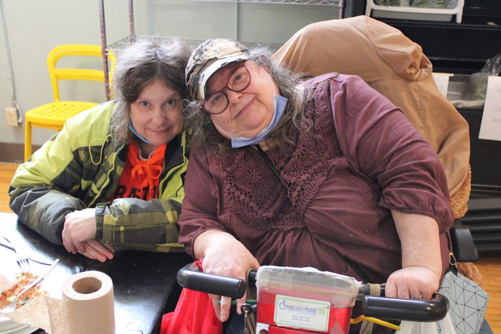 Two women with their masks pulled down pose for a photograph. 