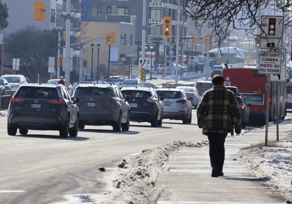 A man walks down a sidewalk Carling. Cars can be seen on the left hand side. 