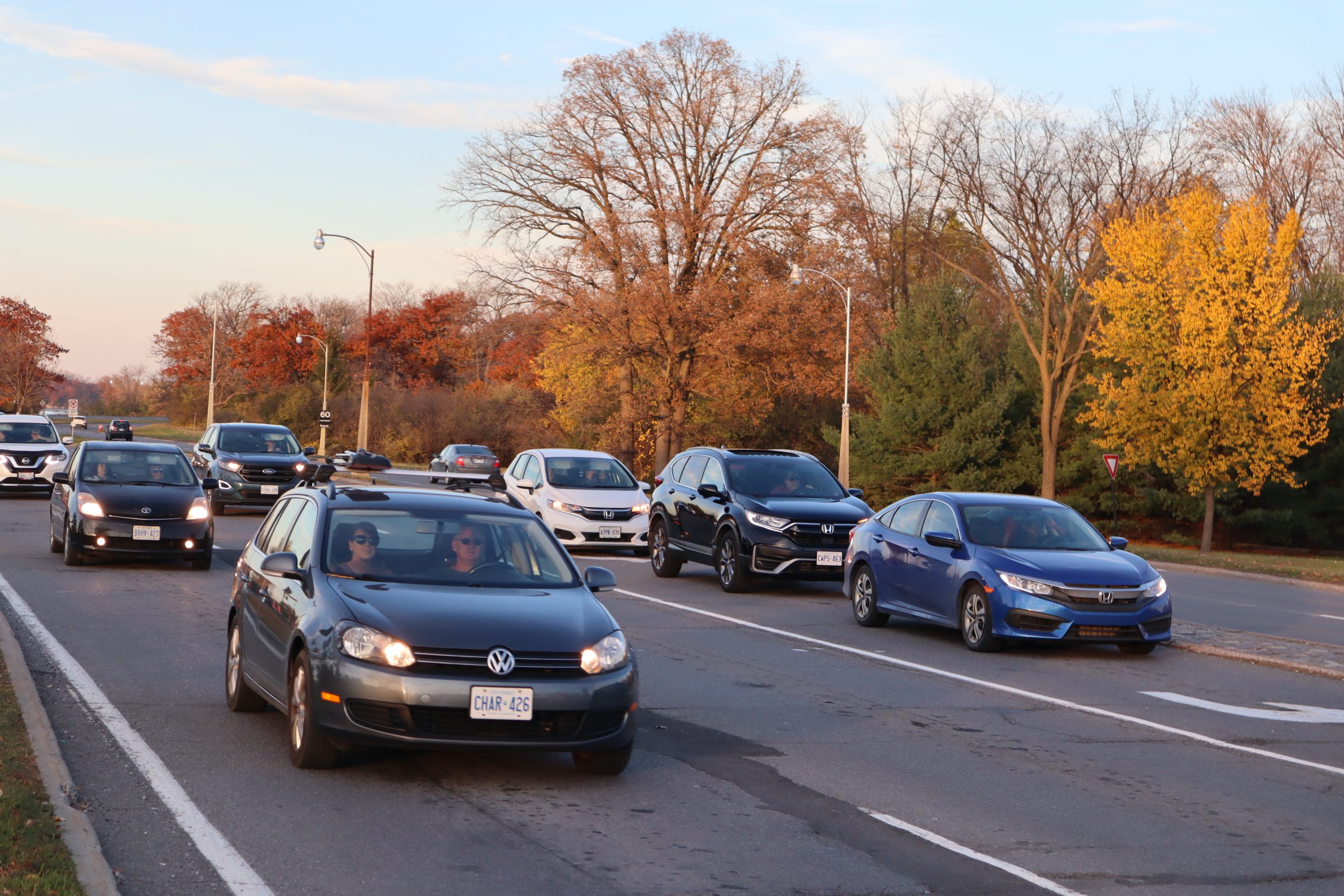 Cars drive down the Sir. John A. MacDonald Parkway. The sun is setting and leaves are changing colours.