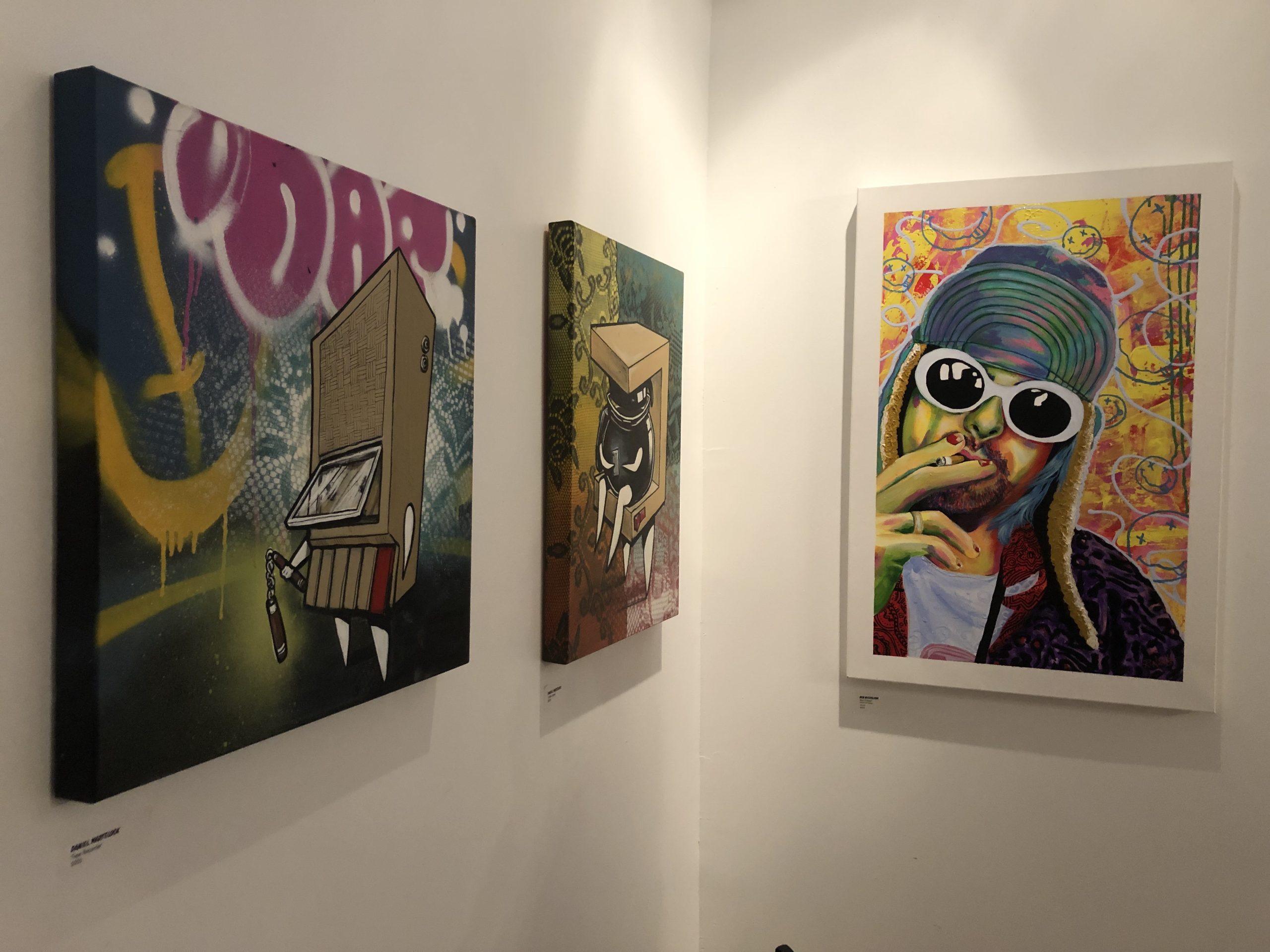 Three colourful paintings hang on a wall.