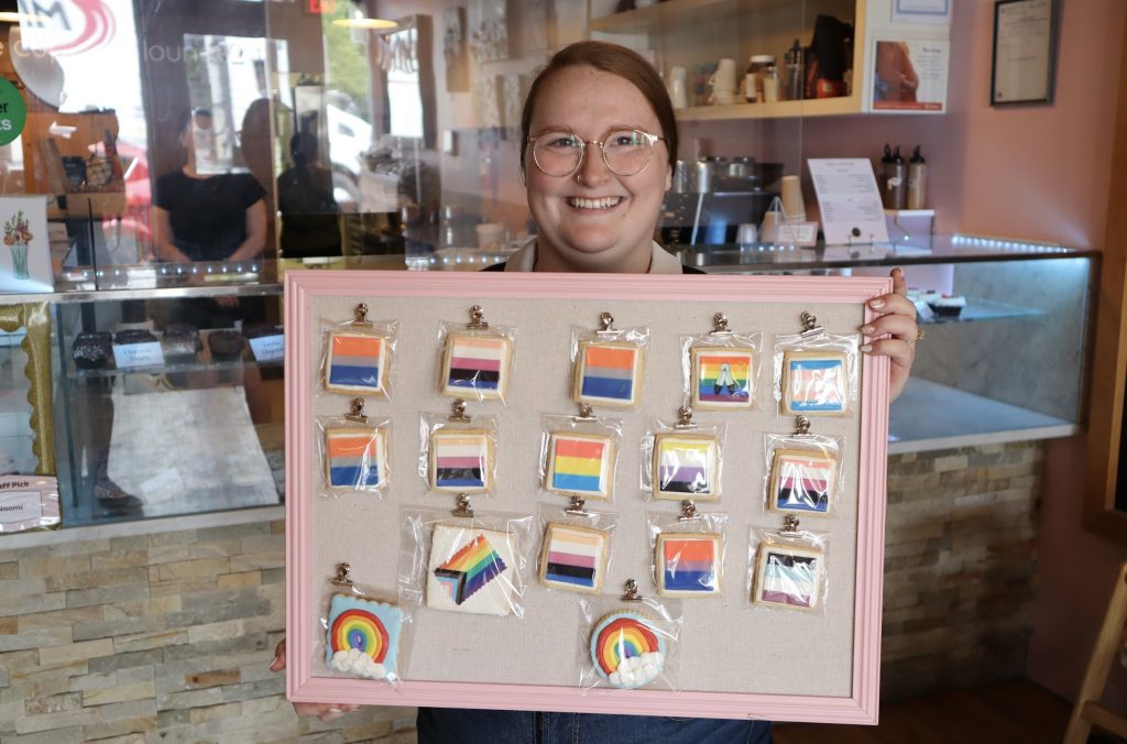 Owner Laura Porter poses for a photograph. She’s holding a board with the various pride flag sugar cookies on display.