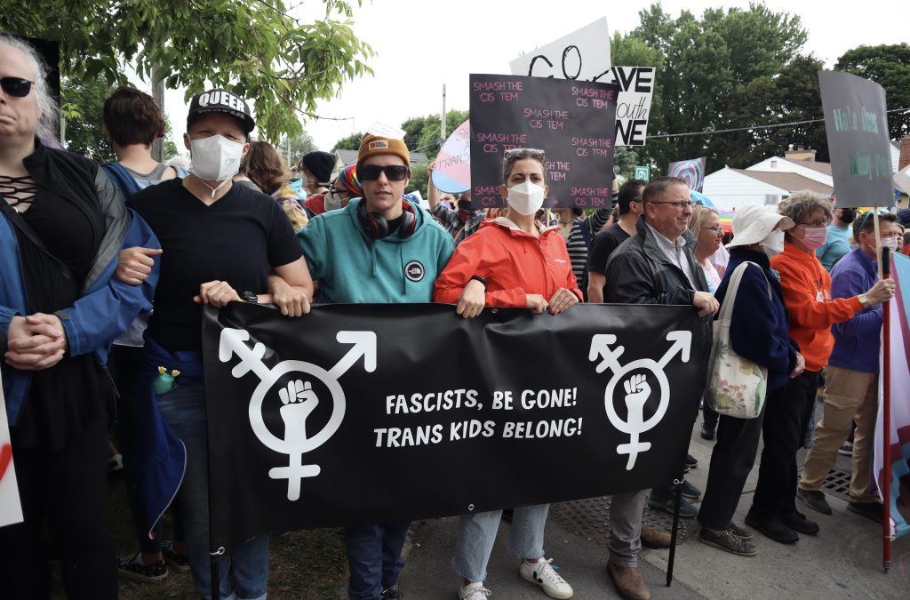 LGBTQ2S+ demonstrators link arms and create a wall of people to stop the right wing group from passing. 