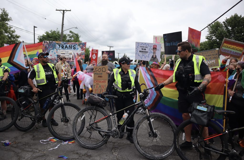 Ottawa Police with their bicycles create a line between the two sides. The LGBTQ2S+ side is seen behind them. 