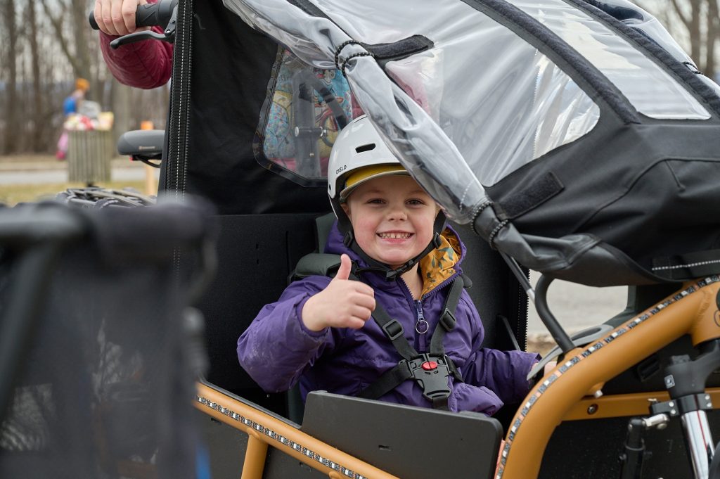 A child gives a thumbs up as he rides in a bike.  