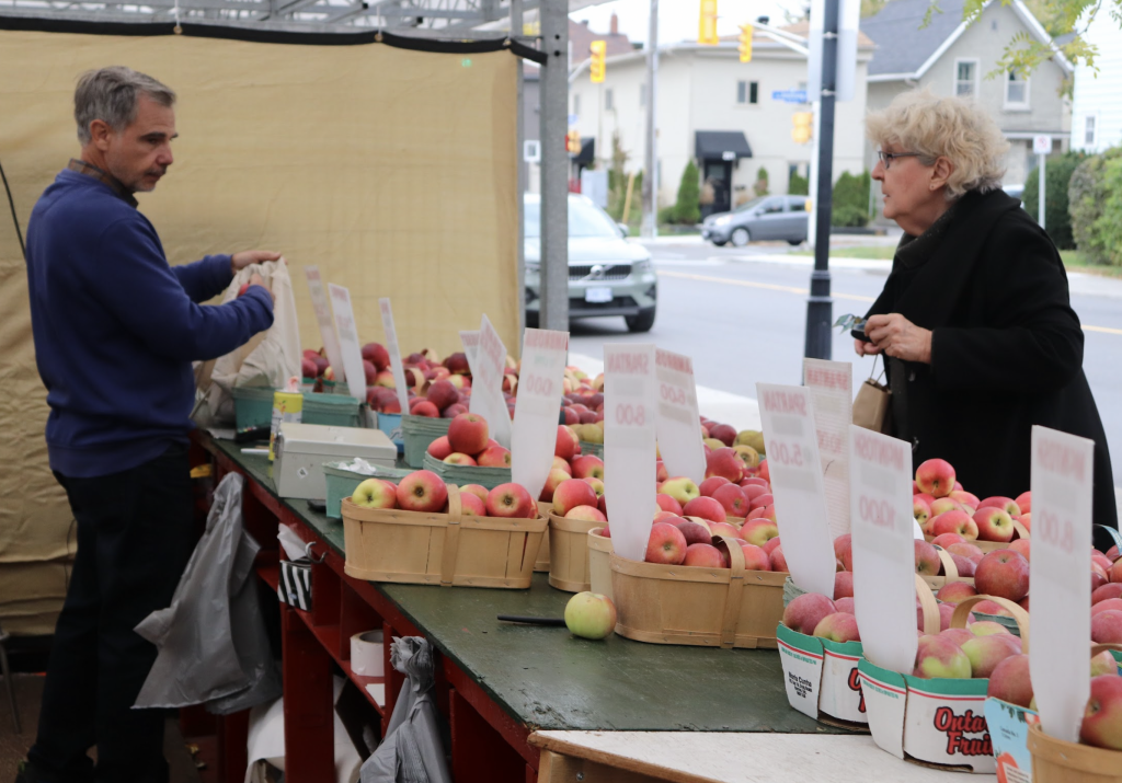 A woman purchases apples from the apple stand. 