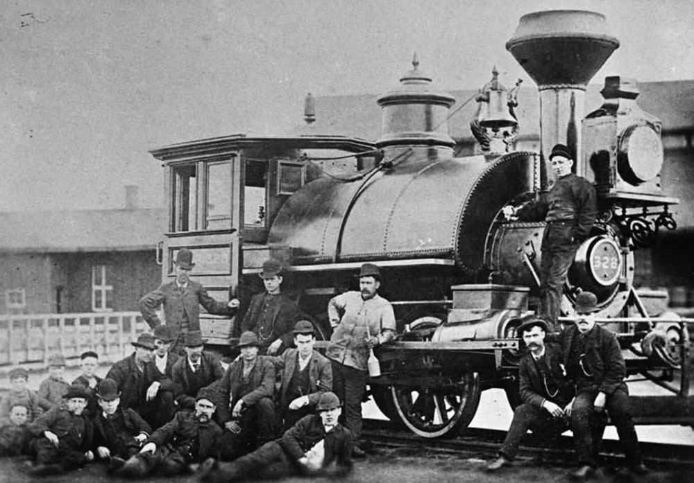 A bunch of men stand next to a steam engine. 