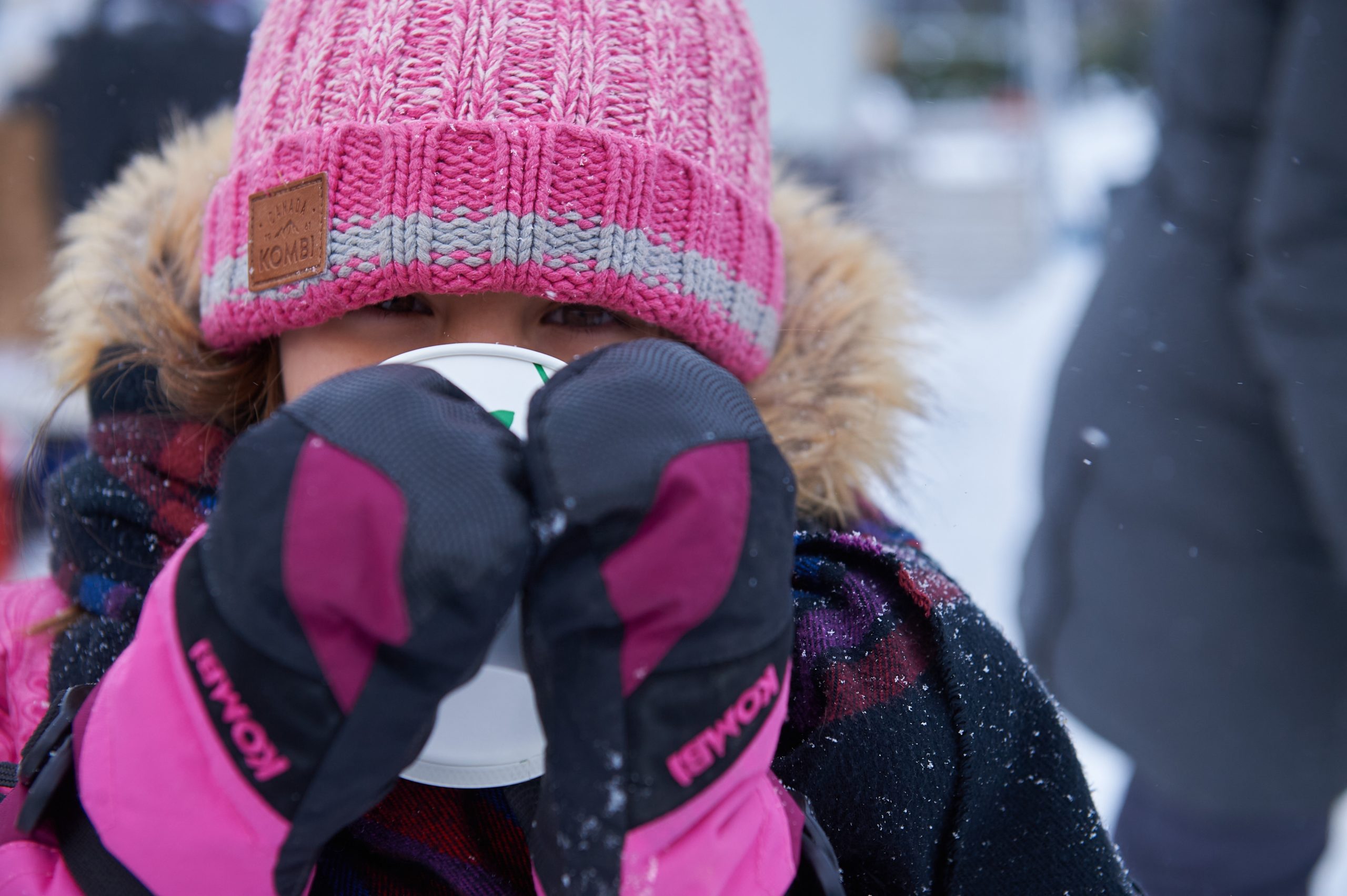 A child in a pink jacket and hat drinks hot chocolate