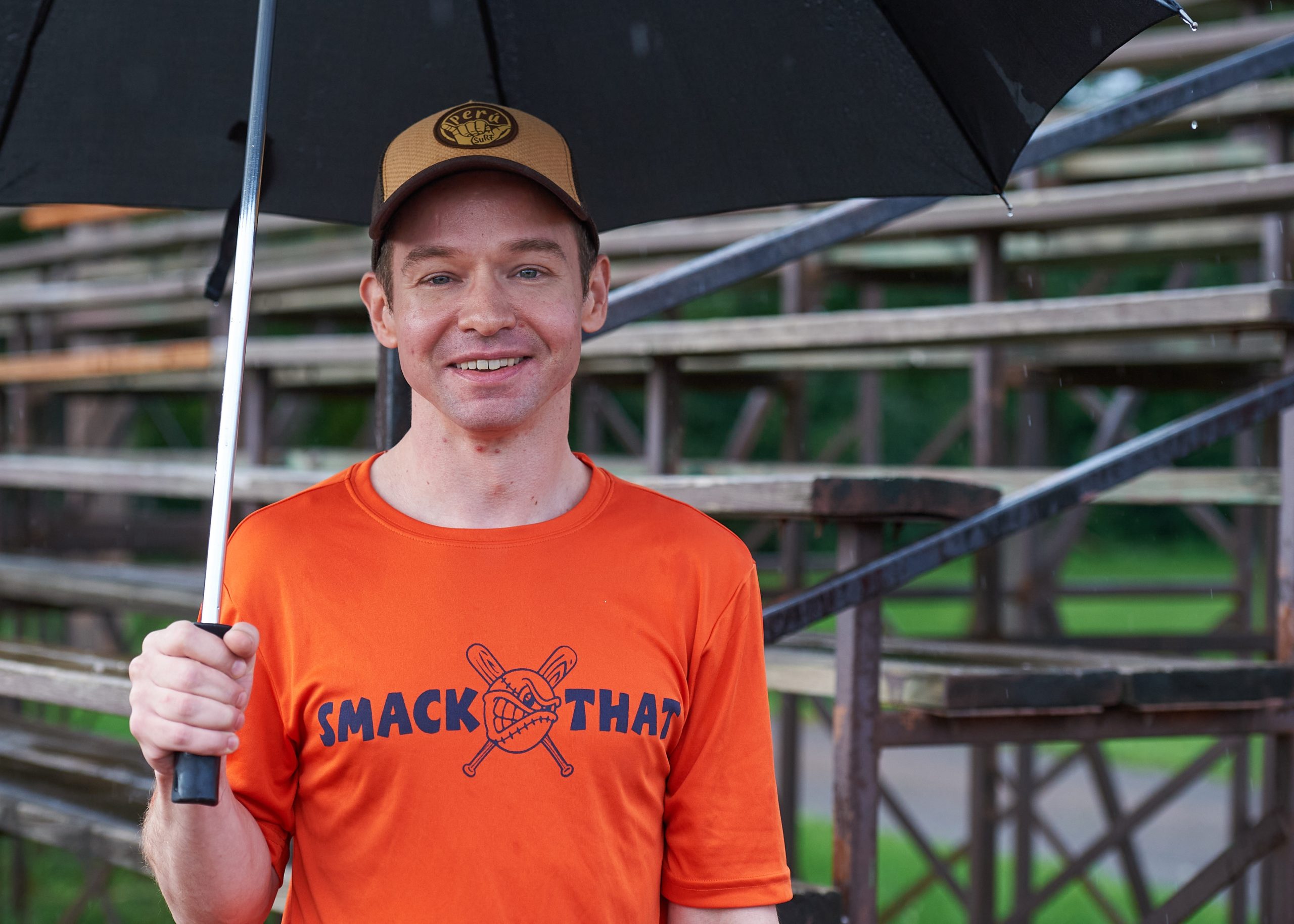 Bradley, wearing an orange shirt, poses for a photograph holding an umbrella. 