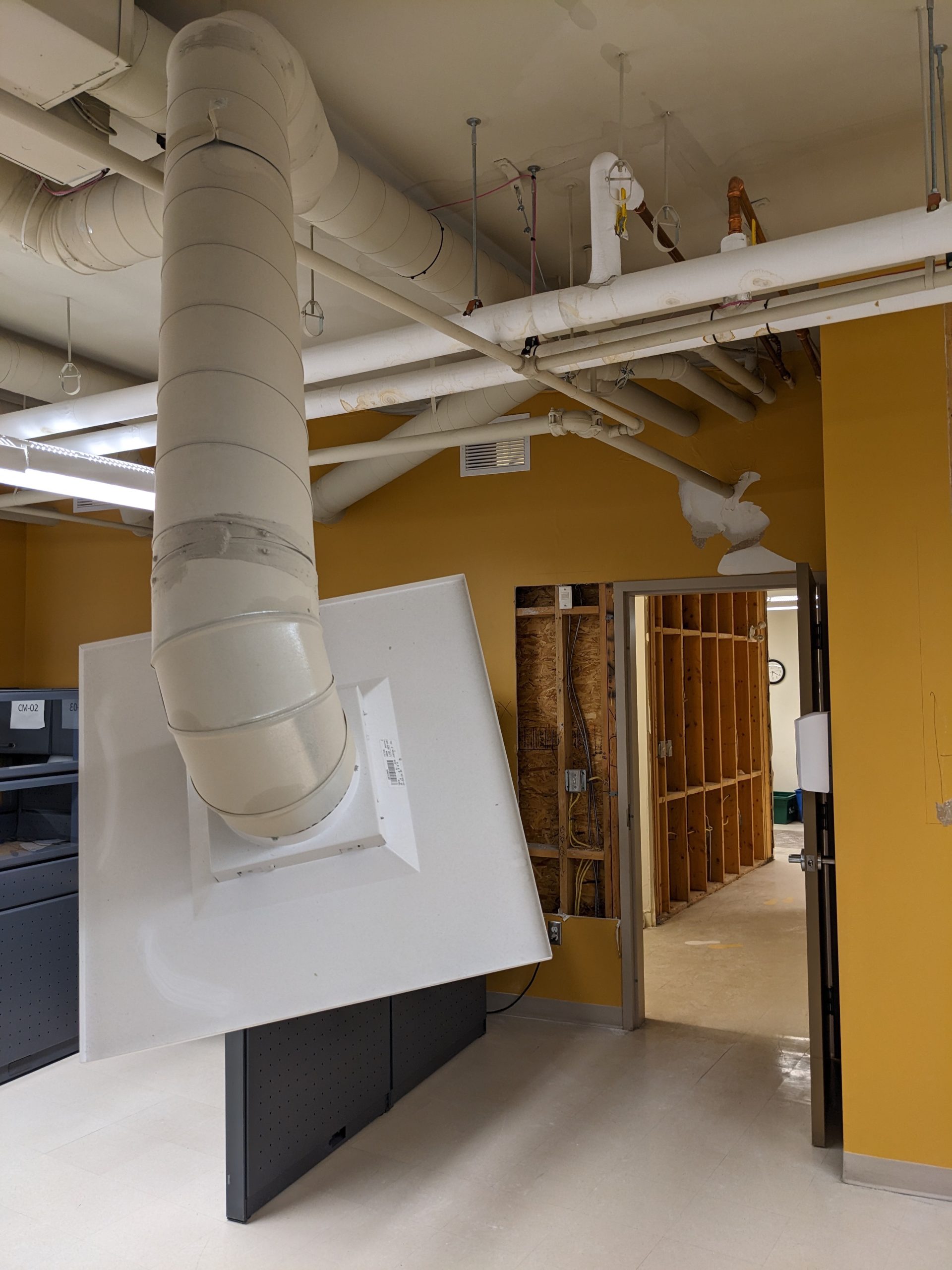 Air duct pieces hang from a falling down ceiling in a room with yellow walls. 
