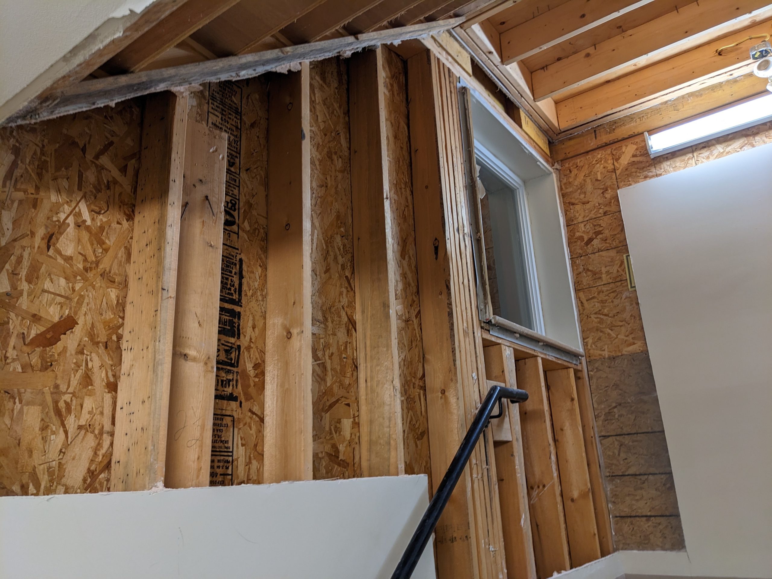 Pieces have drywall have been removed from a wall because of the water damage. A small window is seen at the top of a staircase. 
