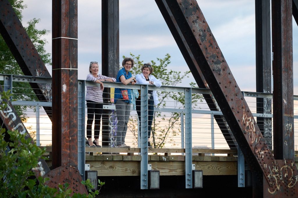 Three women look over the Chief William Commanda Bridge. The sun is setting in the background.