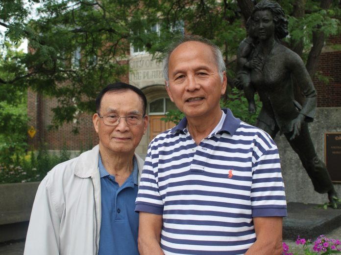 Two men pose for a photo next to a stature at the corner of Somerset and Preston.