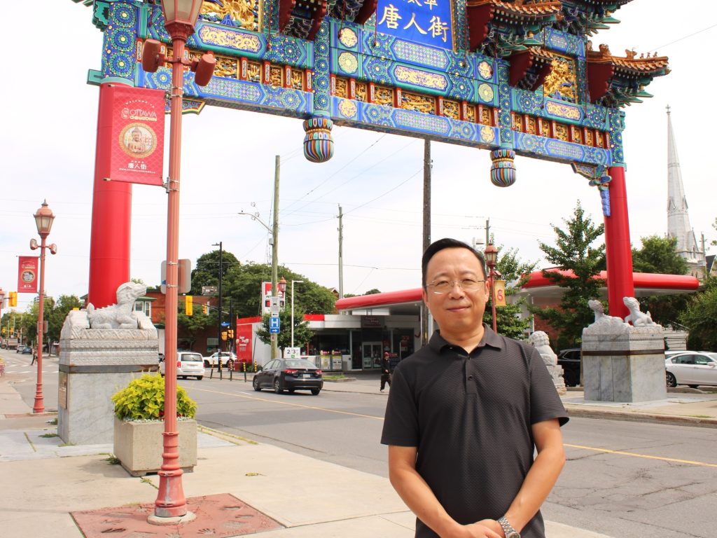 A Chinese man stands next to the Chinatown Archway on Somerset Street.