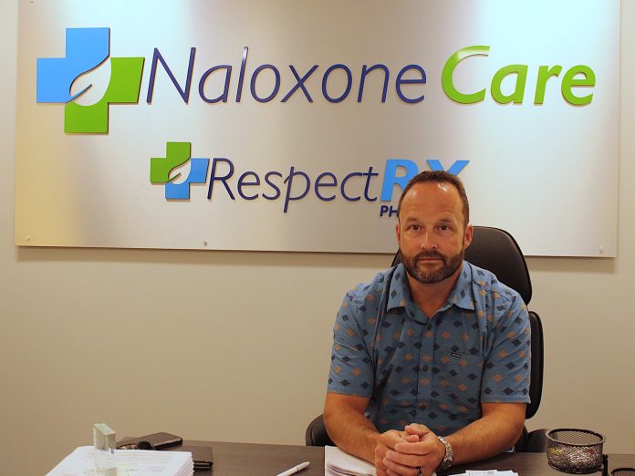 Mark poses for a photo at his desk. A sign promoting his company is overhead.