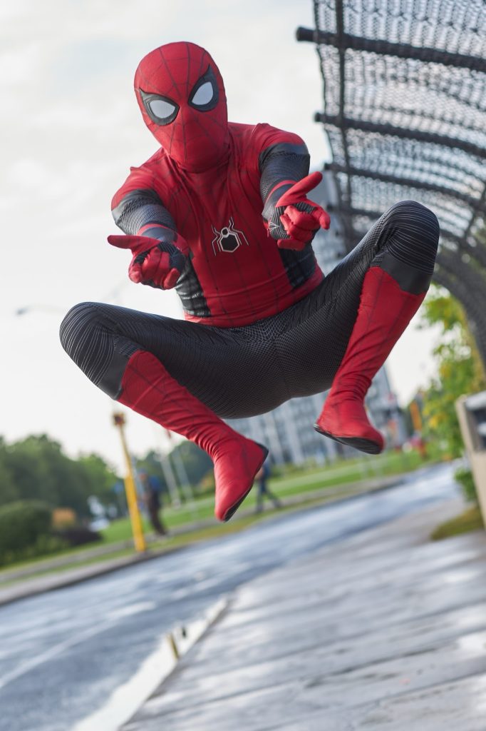 Spider man jumps on a sidewalk and is photographed mid air. Tunneys pasture is seen in the distance.