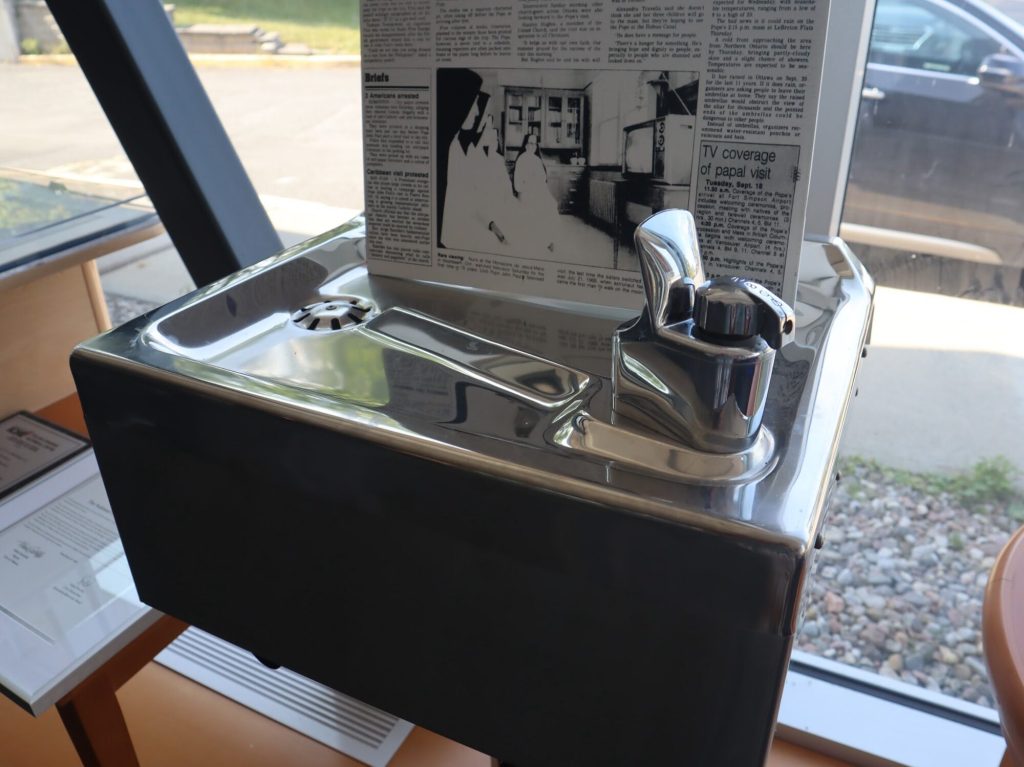 An old water fountain sits next to a window.