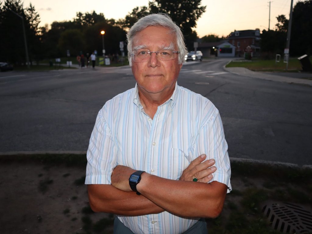 Alex poses for a photo on a residential street with his arms crossed.