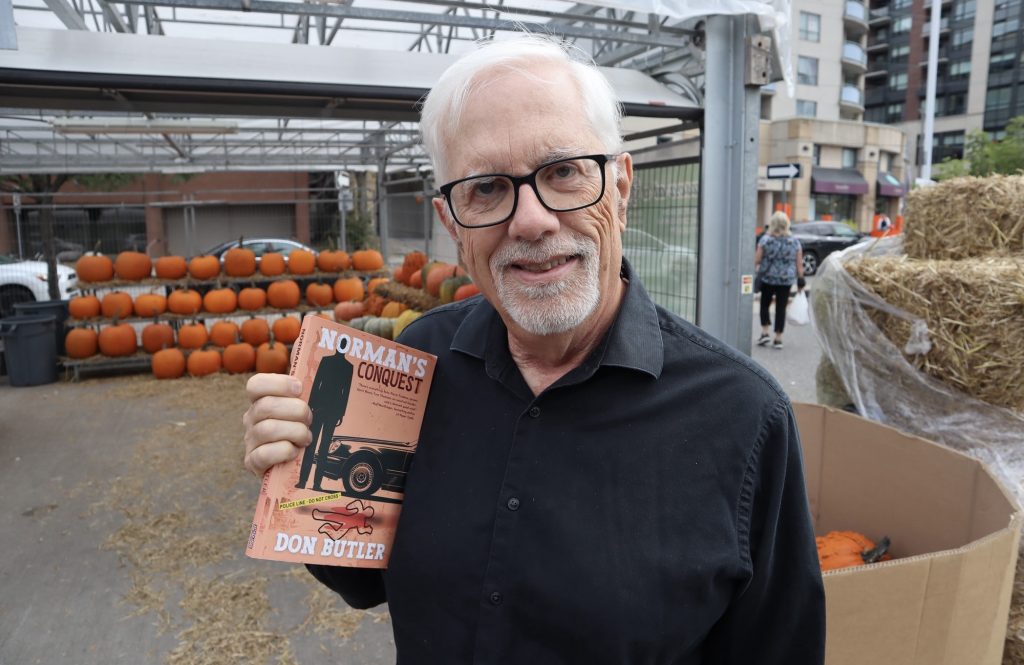 Don holds his book near a pumpkin stand.