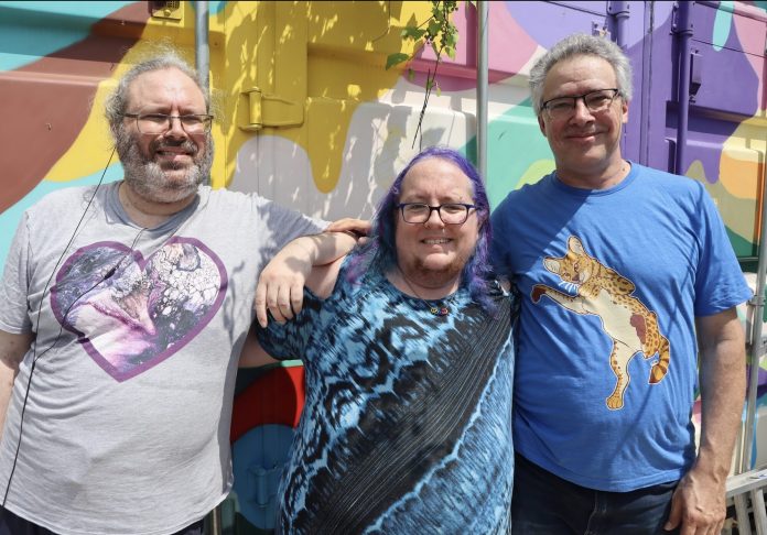 Three people pose for a photo next to a colourful shipping container.