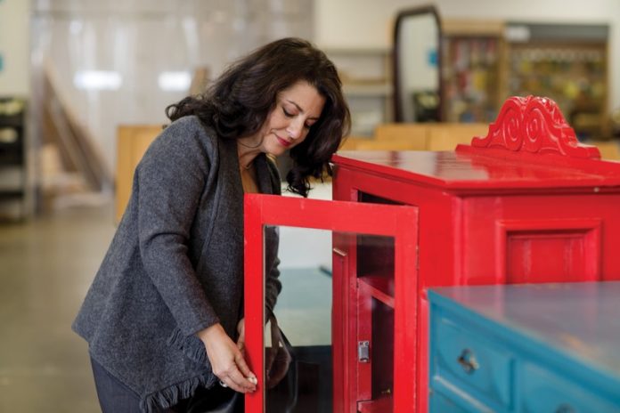 A woman opens up a red cabinet.