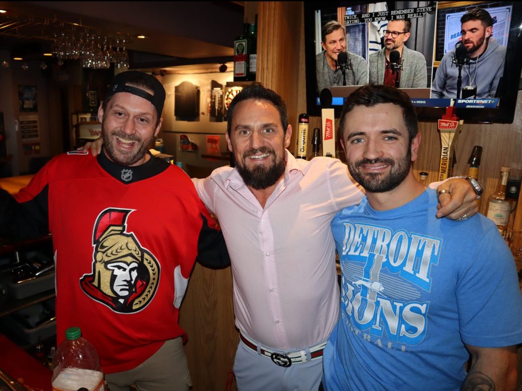 Three people pose for a photograph behind a bar.