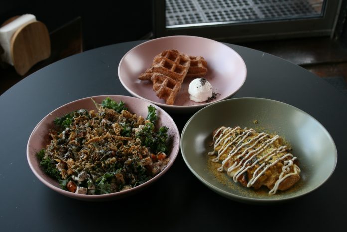 Three plates of food sit on a table. Two appear to be salads and the middle is a croffle.